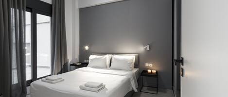 A modern bedroom with a large bed, bedside tables with lamps, and a view through a window with curtains.