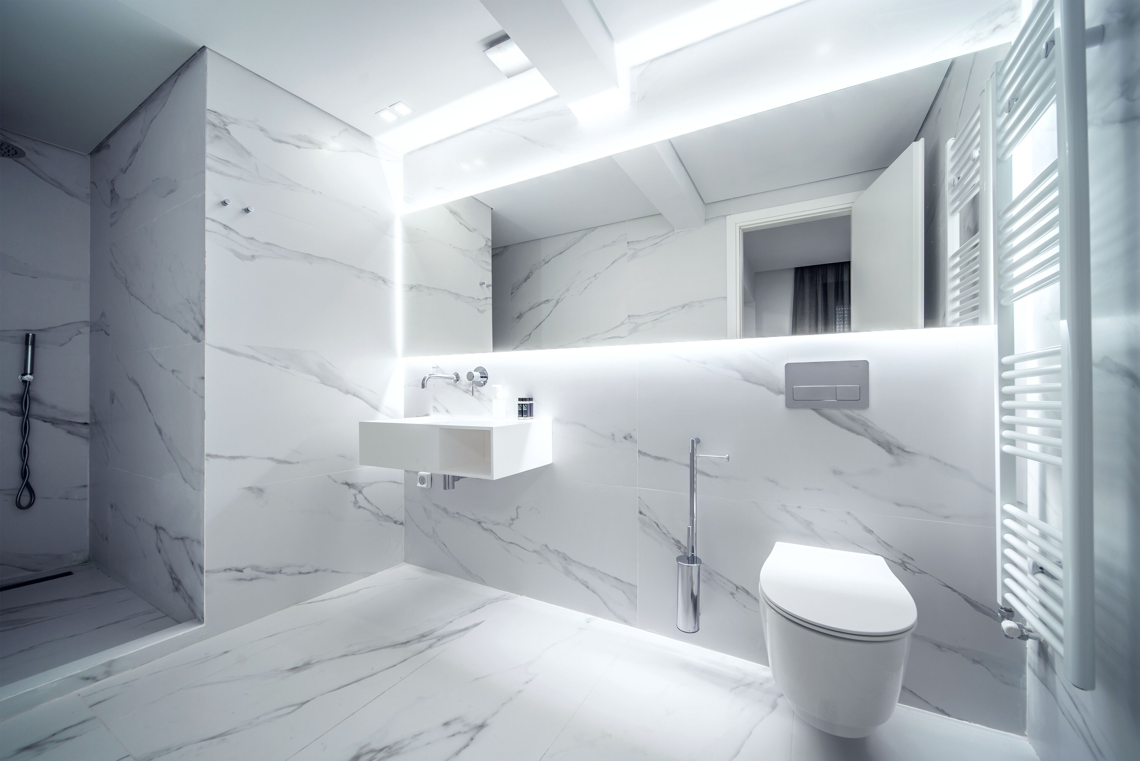 Et moderne badeværelse med klinkegulv af marmor, et hvidt håndvaskarrangement, toilet og bruseområde.