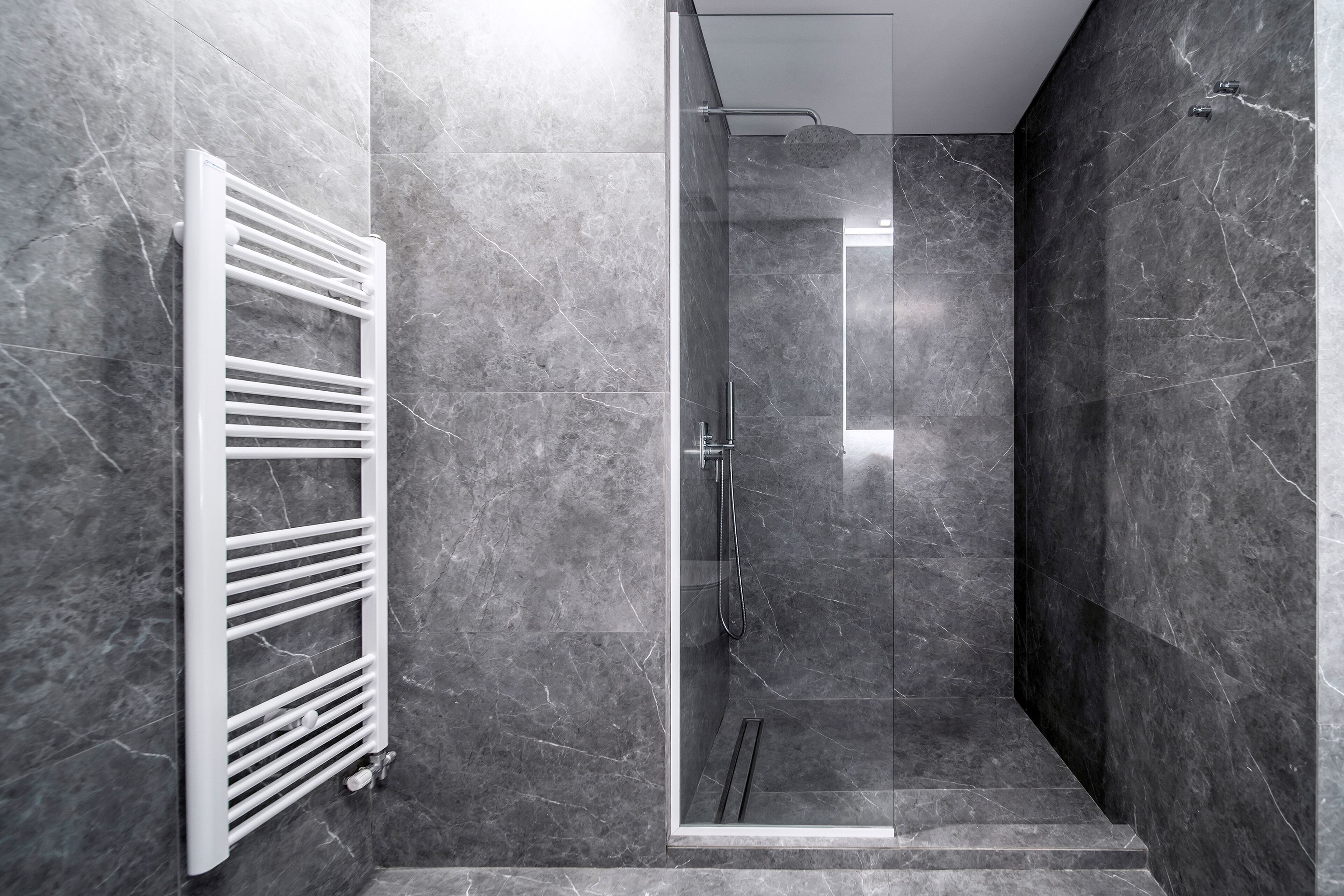 Un baño moderno con ducha de vidrio, toallero blanco y paredes de mármol.