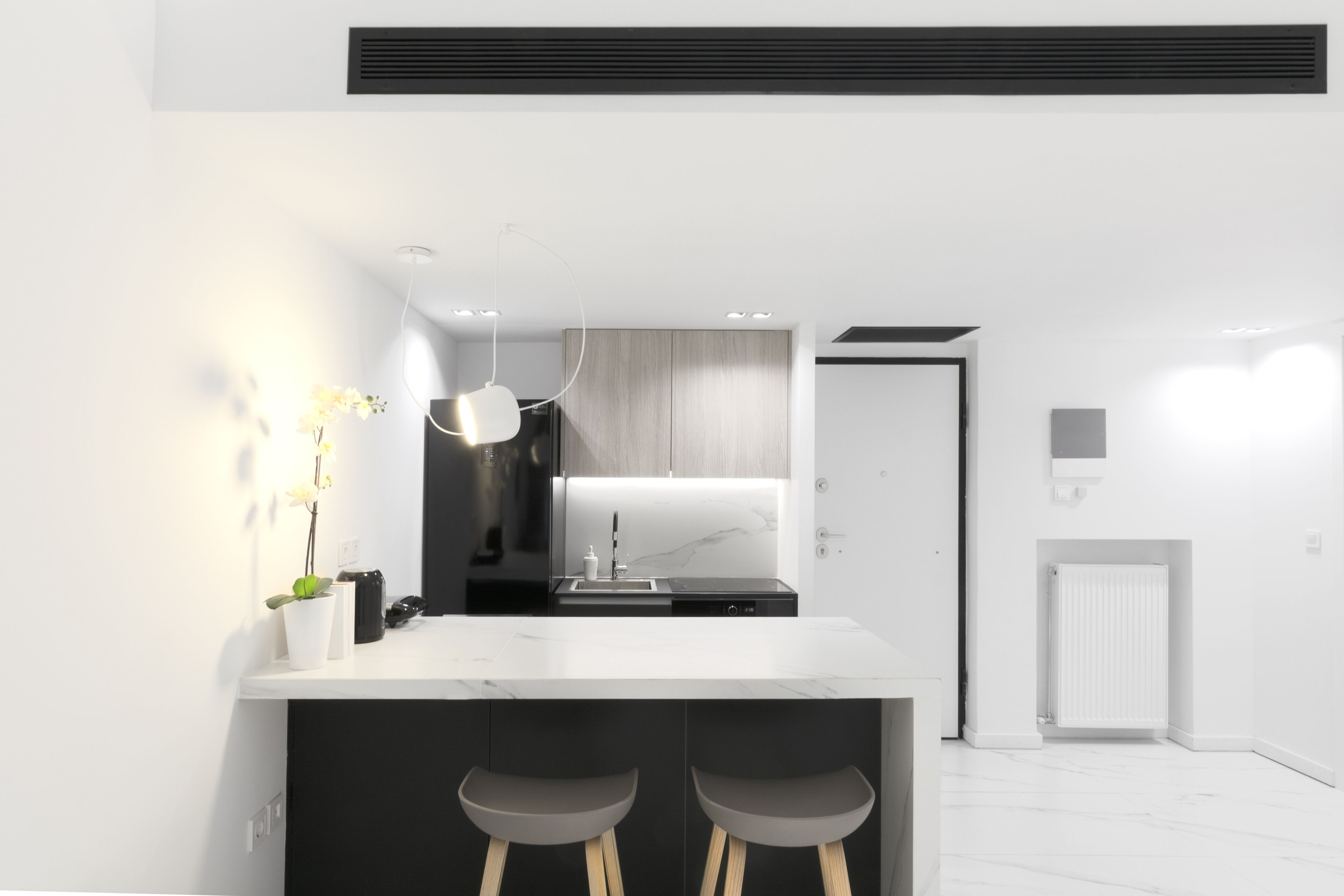 Et moderne køkken med en hvid bordplade, sorte barstole og en hængende lampe.