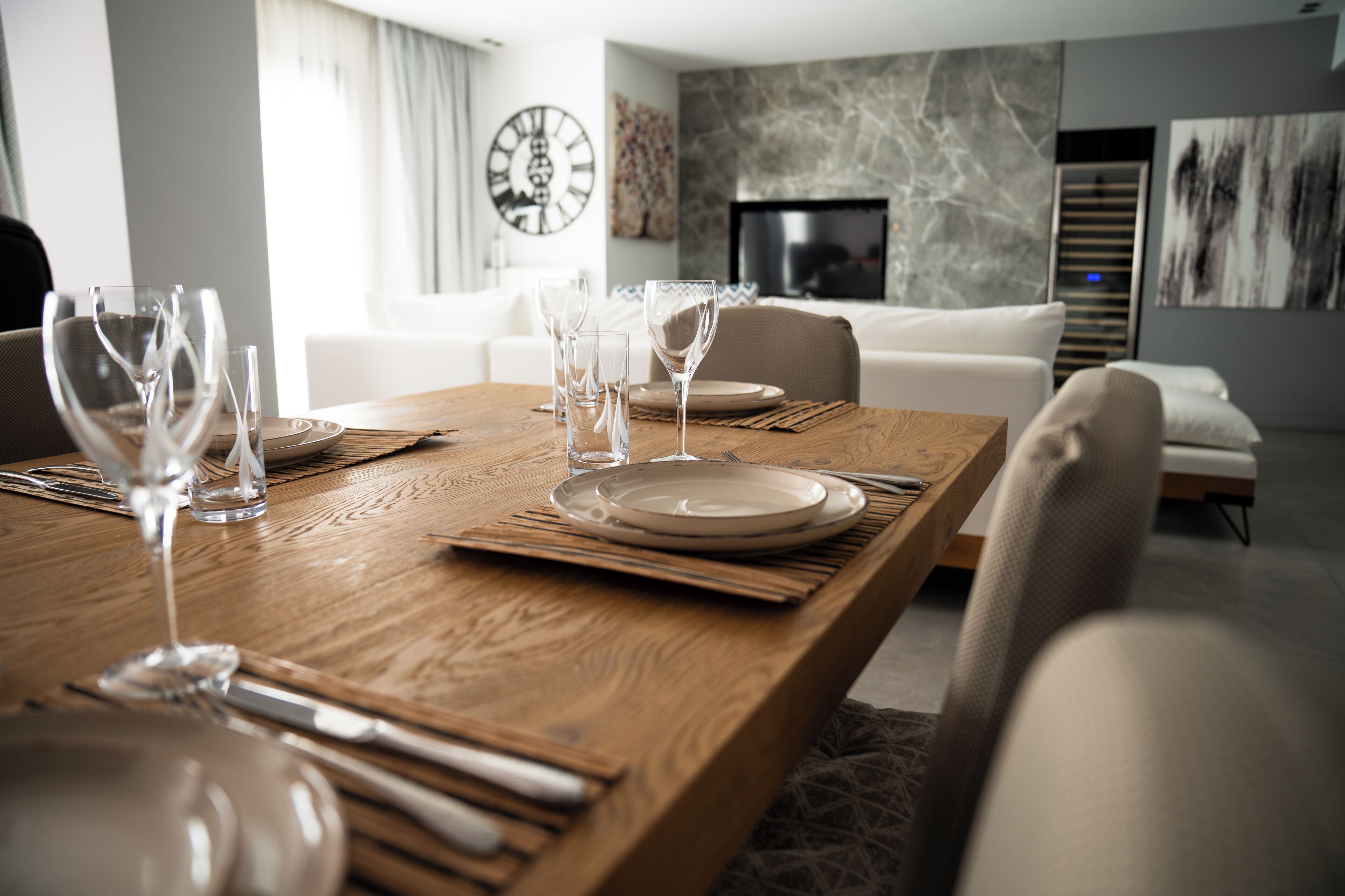 A dining table set with plates, glasses, and cutlery, with a modern living area in the background.