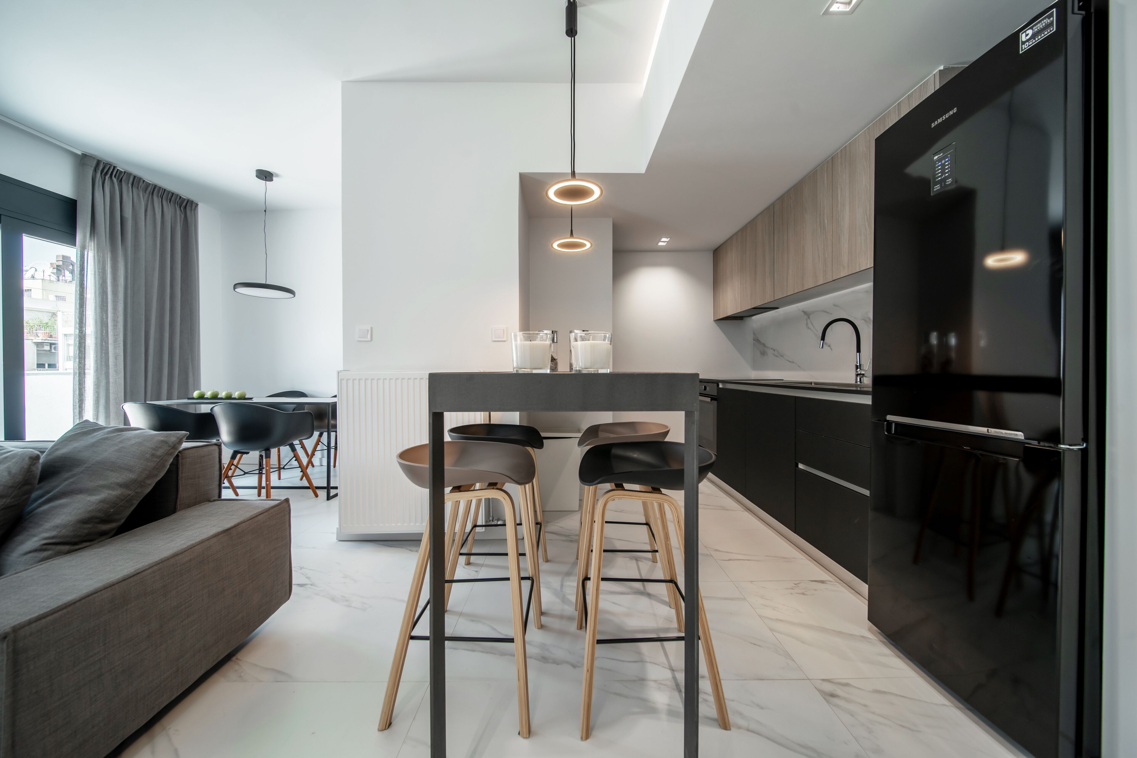 Une cuisine moderne avec un îlot central, un réfrigérateur noir et des tabourets en bois.