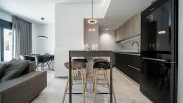 A modern kitchen with a central island, black refrigerator, and wooden stools.