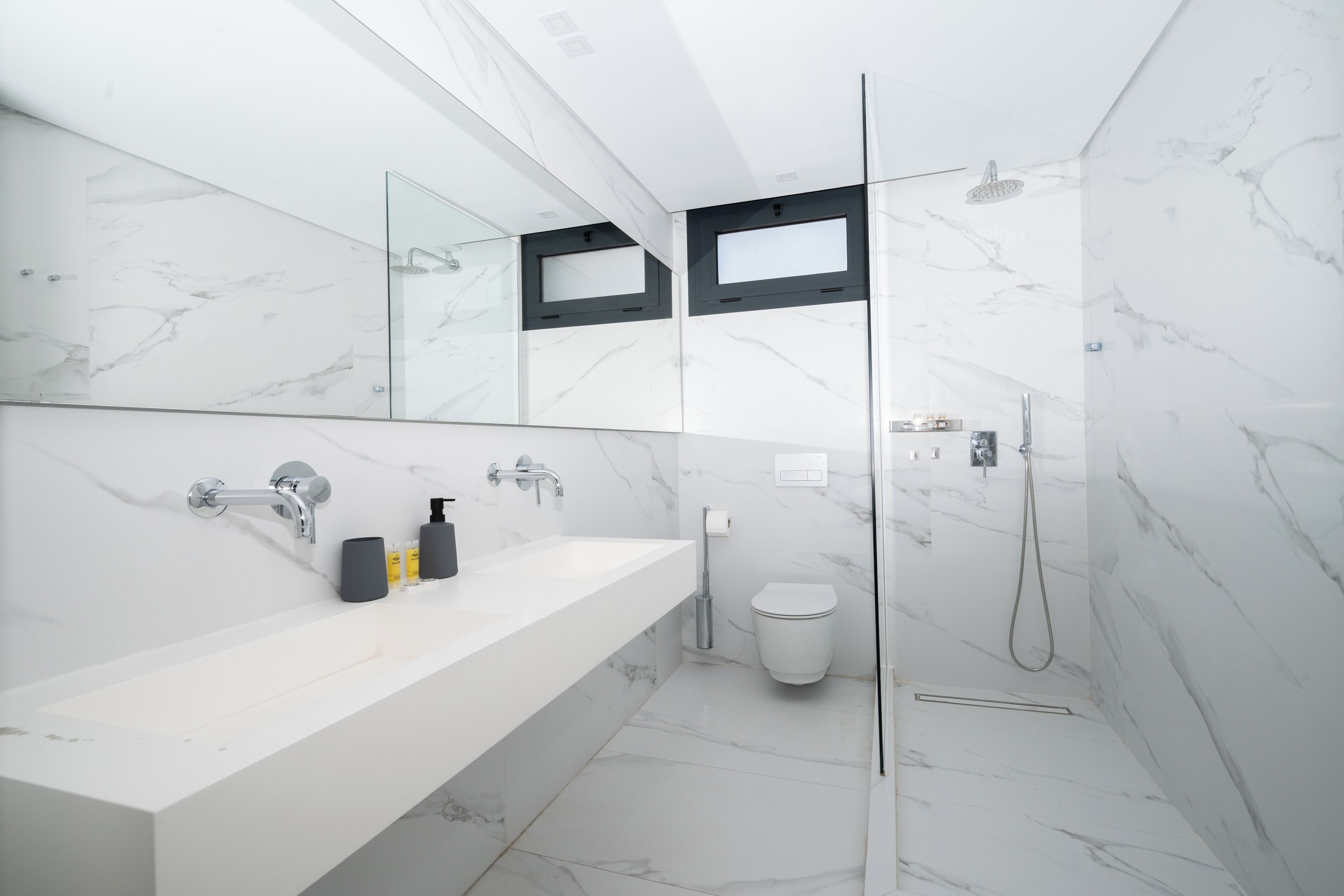 Une salle de bain moderne avec un lavabo en marbre blanc, un grand miroir et une douche à parois de verre.