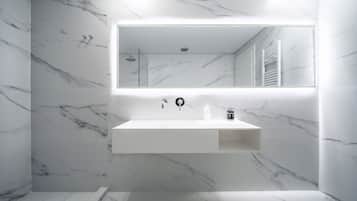 Un baño moderno con pared de mármol, un espejo grande, un lavabo blanco y zona de ducha.