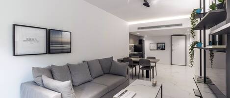 A modern living room with a grey sofa, a coffee table, and a dining area with chairs and a table.