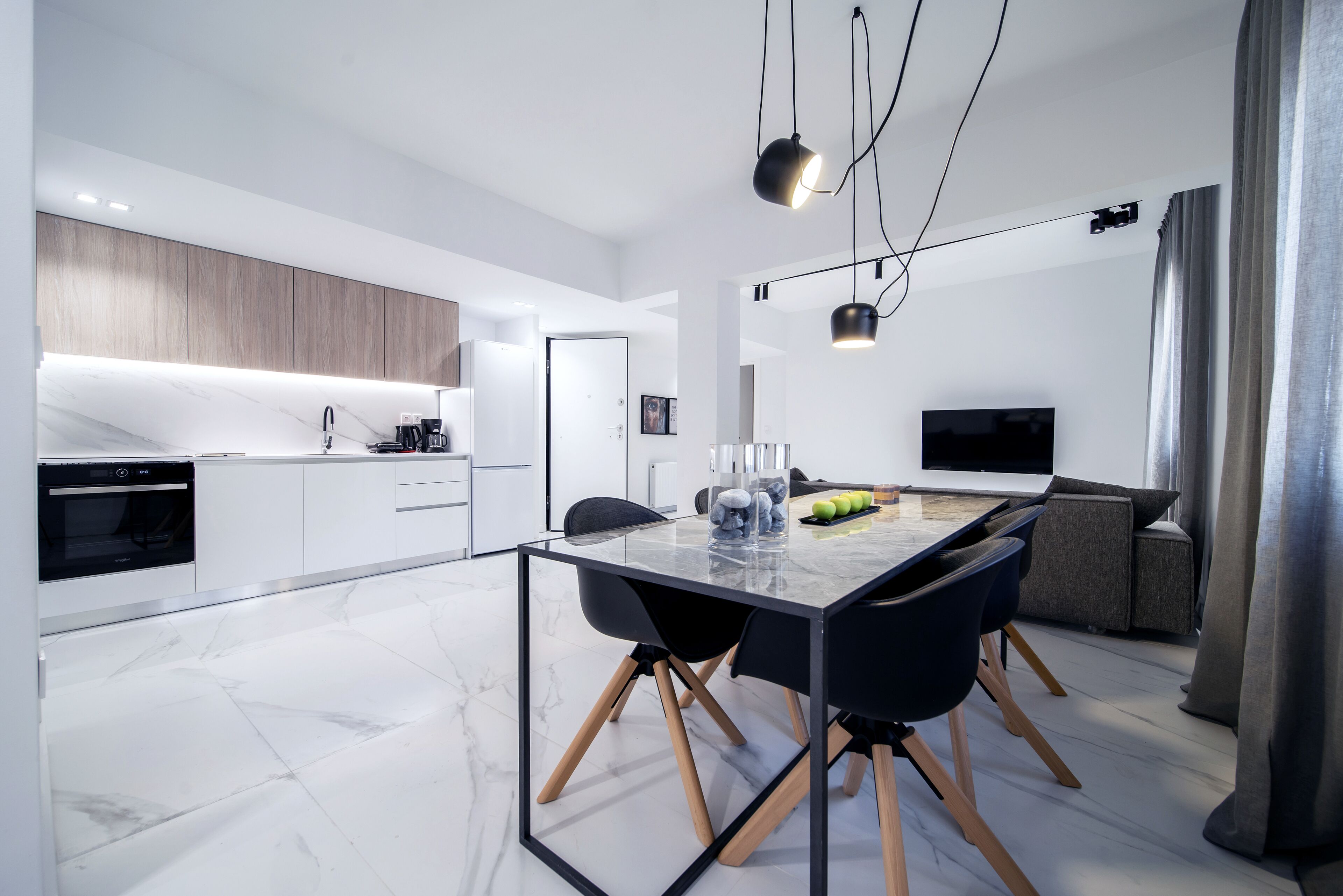 Una cocina moderna con armarios blancos, horno empotrado y comedor con mesa de vidrio y sillas.