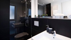 Un baño moderno con ducha de vidrio, un lavamanos blanco y un espejo encima.