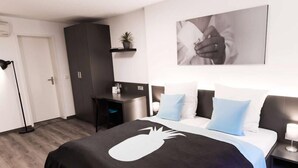 Una habitación de hotel moderna con una cama, un escritorio, un armario y un estante en la pared con una planta.