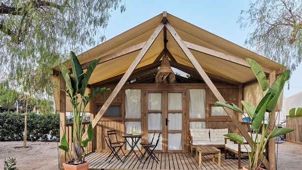Una estructura de madera con techo triangular, un porche cubierto con mesa y sillas, y plantas en macetas.