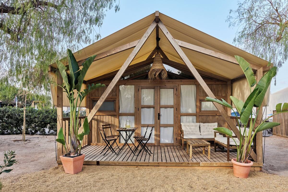 Eine Holzhütte mit einem dreieckigen Dach, einer überdachten Terrasse mit Tisch und Stühlen sowie Topfpflanzen.