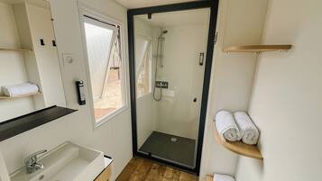 A modern bathroom with a glass-enclosed shower, a white sink, and wooden shelves holding towels.