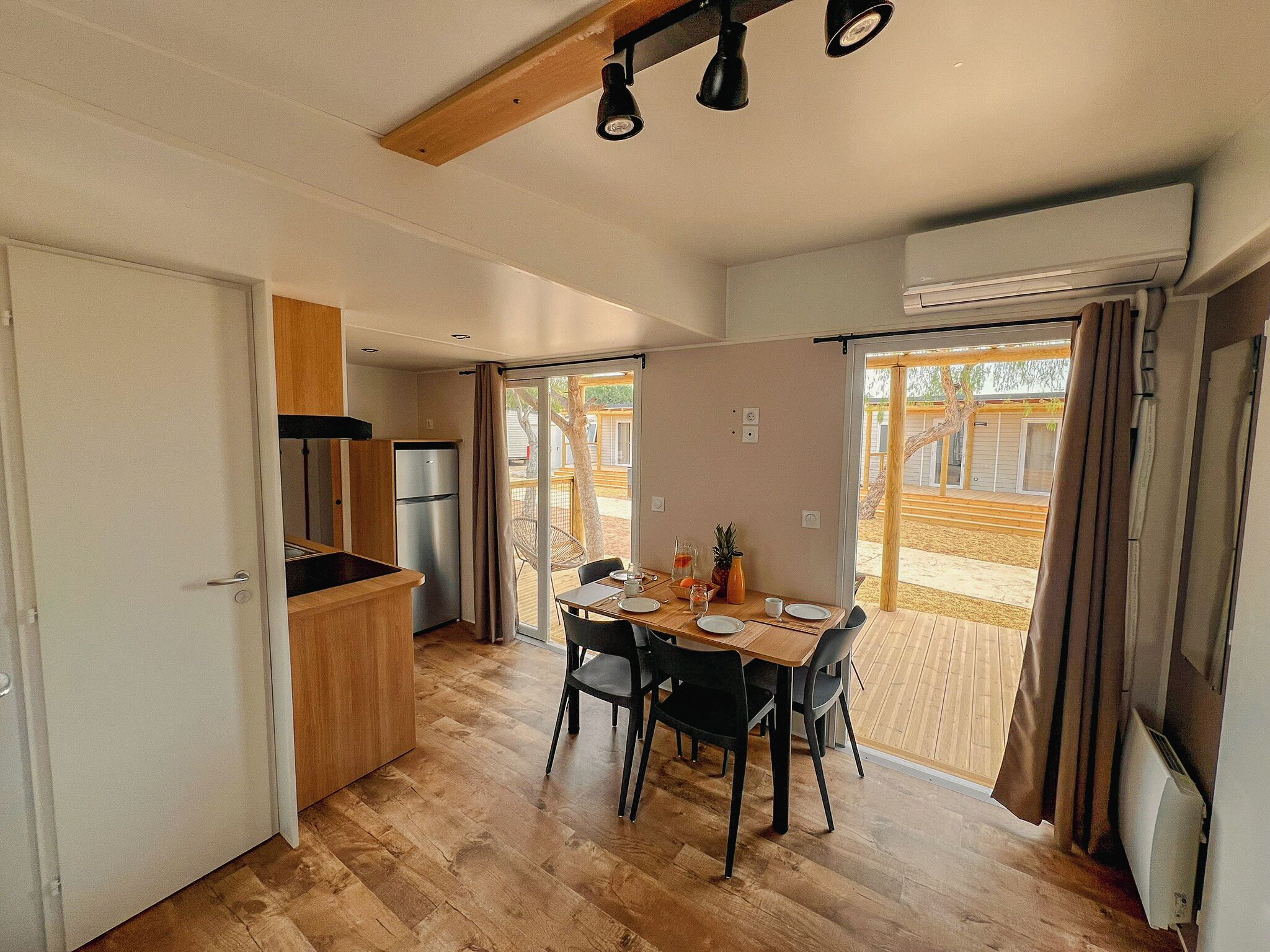A compact kitchen with a dining area, wooden flooring, and a sliding glass door leading to an outdoor patio.