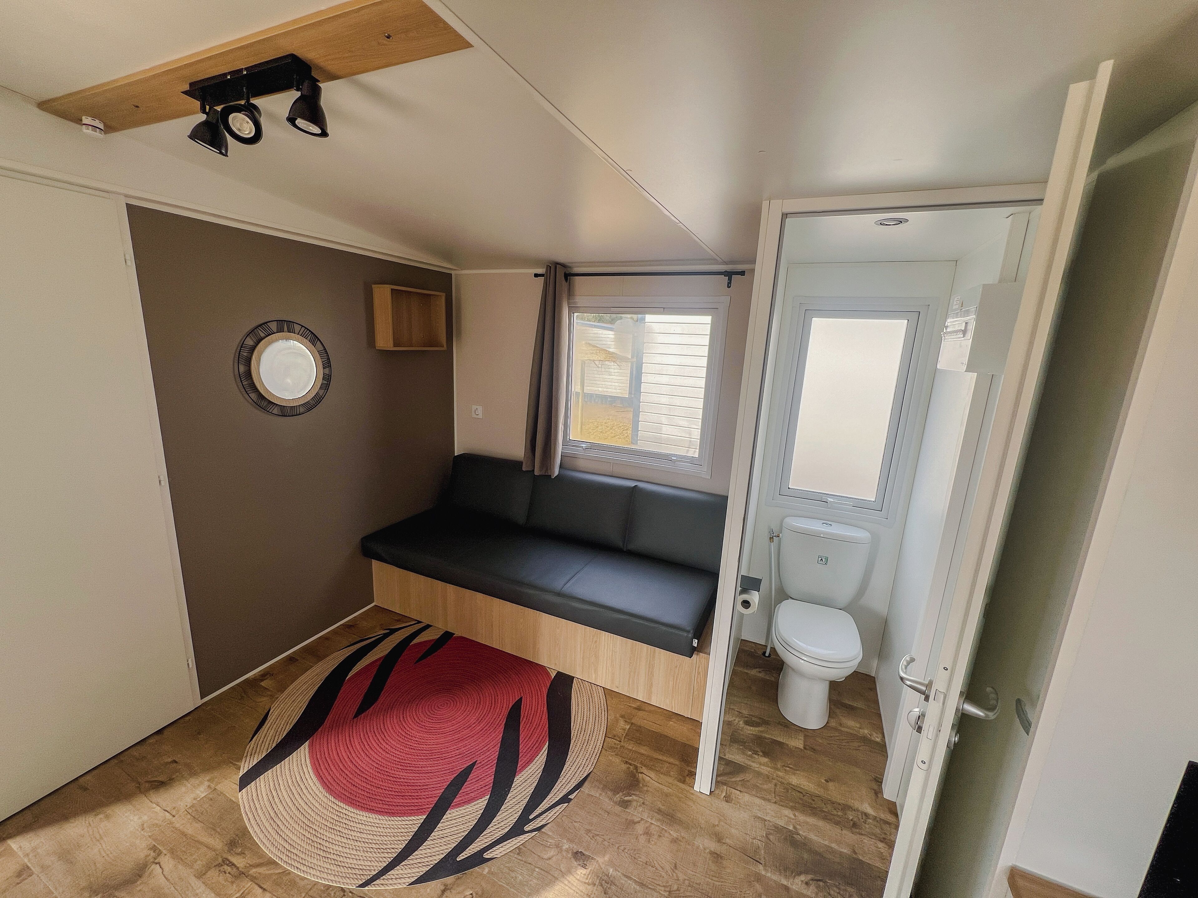 Un baño moderno y compacto con un asiento de banco, un inodoro y un ventanal.