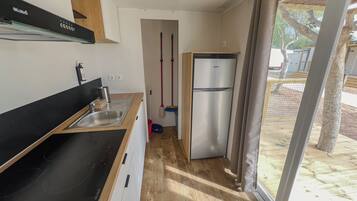 Eine kompakte Küche mit Spüle, einer schwarzen Arbeitsplatte, einem Edelstahlkühlschrank und Blick ins Freie durch eine Glastür.