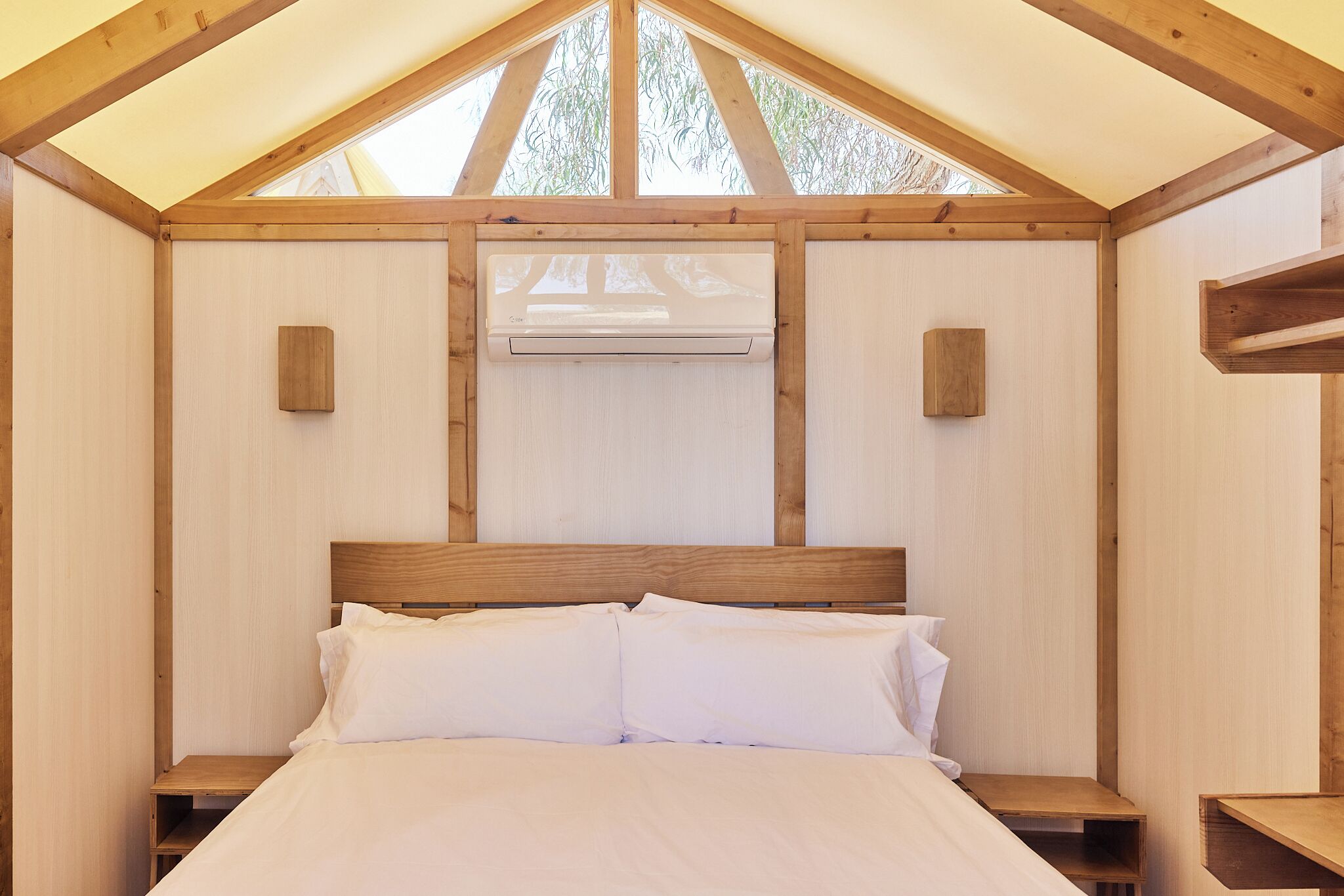 A wooden bedroom with a bed, two bedside tables, and an air conditioning unit.