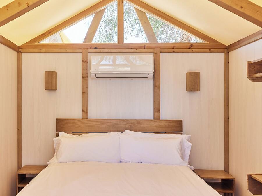 A wooden bedroom with a bed, two bedside tables, and an air conditioning unit.