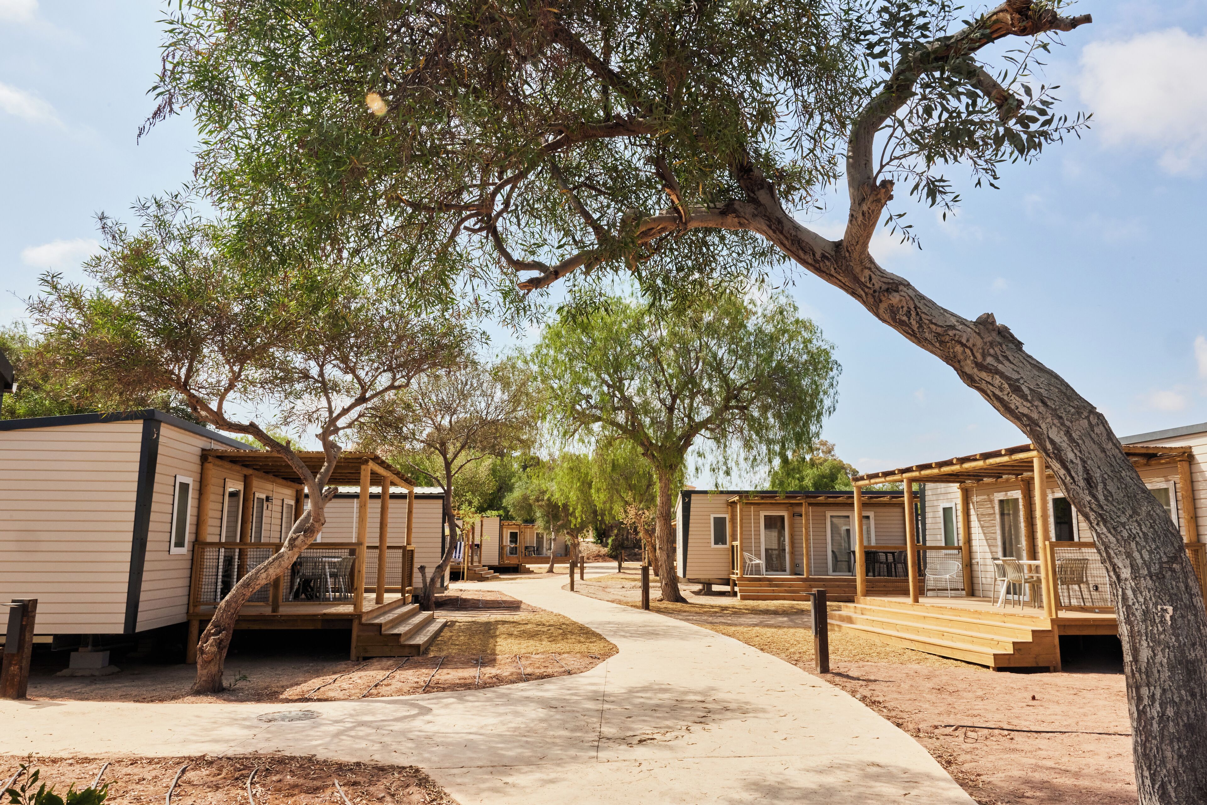 Una hilera de casas móviles con terrazas de madera y zonas de estar al aire libre, unidas por un camino de hormigón.