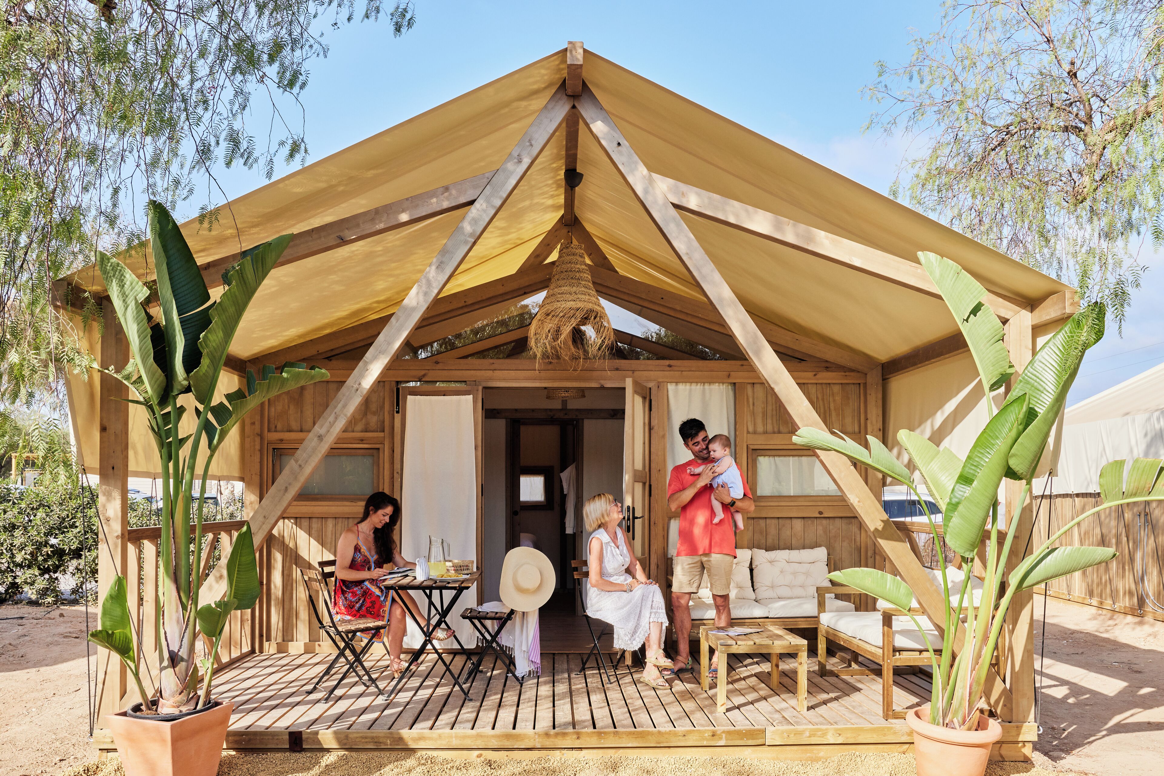 Una estructura de madera con techo triangular, una zona de comedor con mesa y sillas, y plantas en macetas.