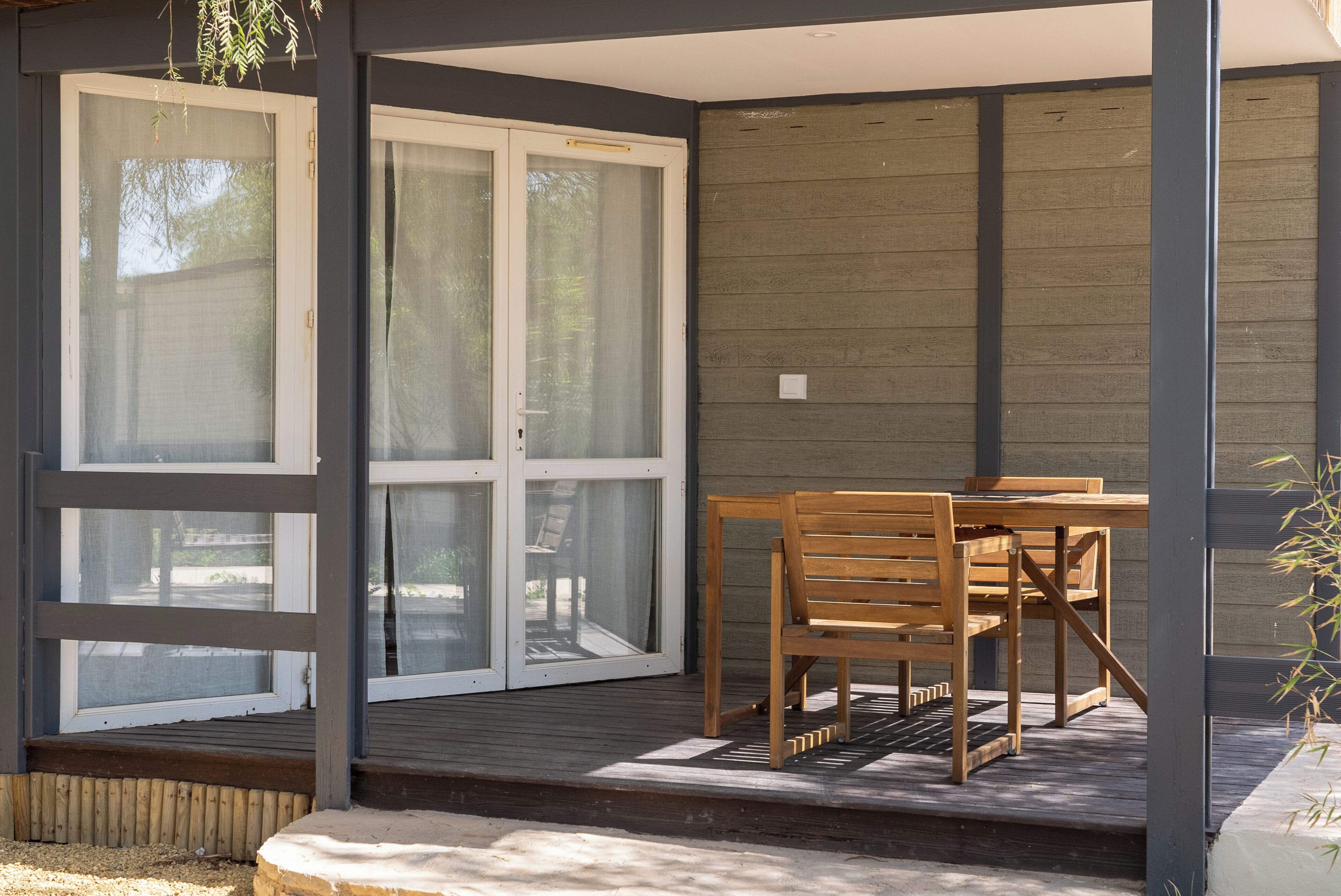 Un patio cubierto con una mesa y sillas de madera, una puerta corrediza de vidrio y una terraza de madera.