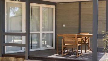 Un patio cubierto con una mesa y sillas de madera, una puerta corrediza de vidrio y una terraza de madera.