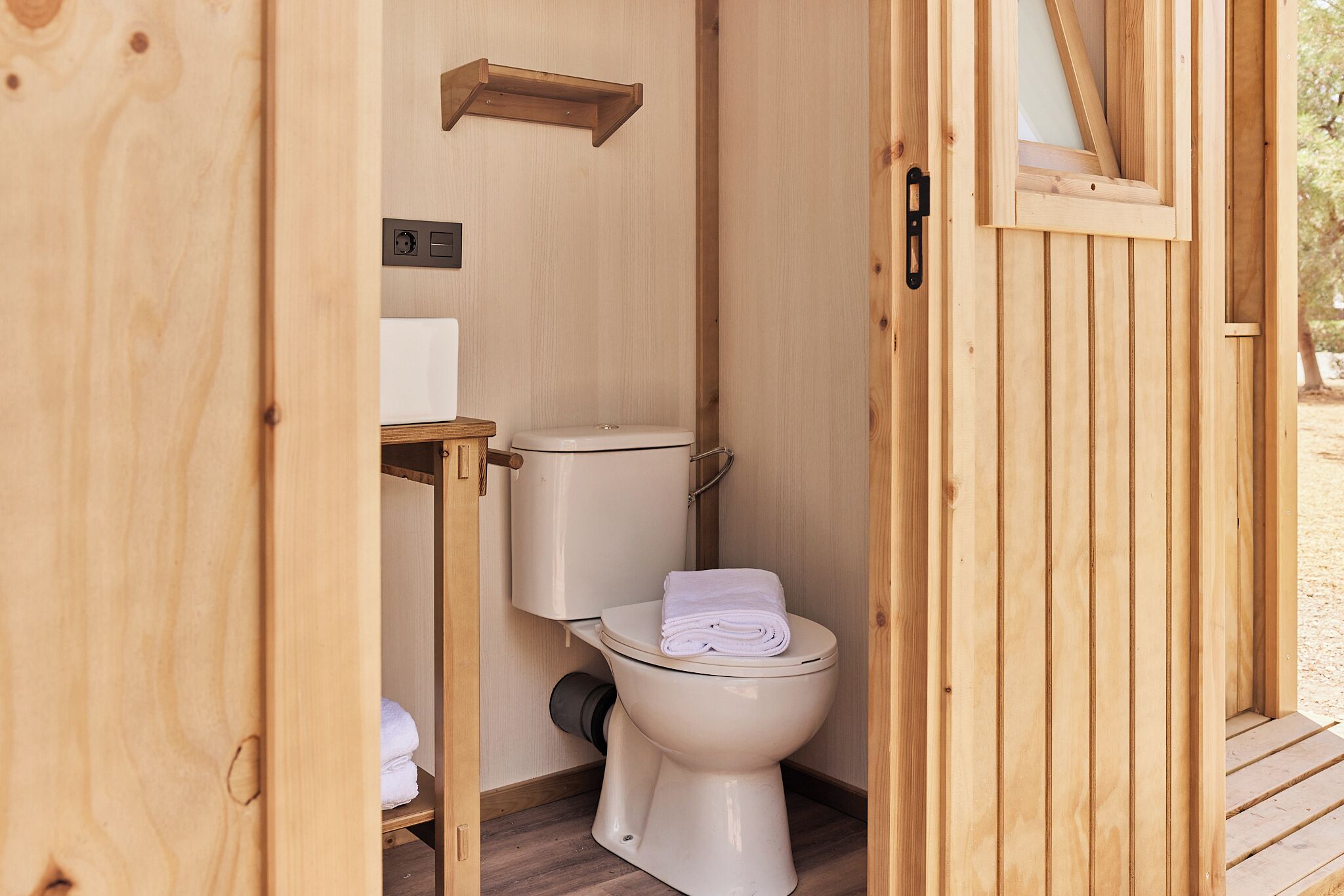 Een houten badkamer met toilet, een plank en een raam.
