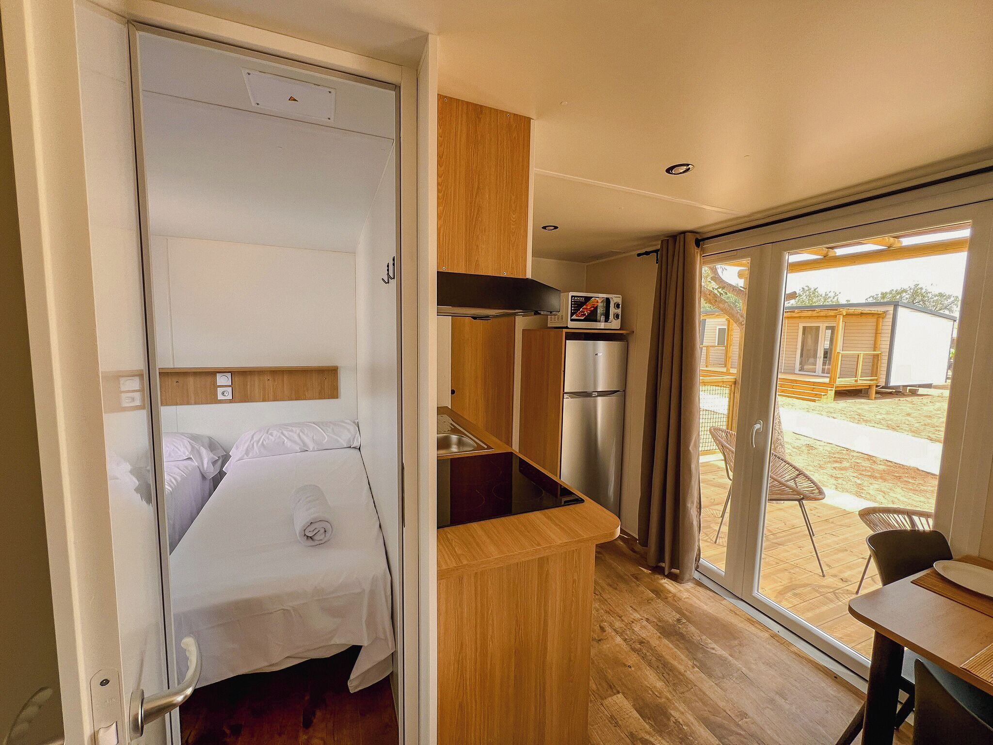Een compacte kamer met een bed, een kitchenette en een glazen schuifdeur naar een buitenruimte.
