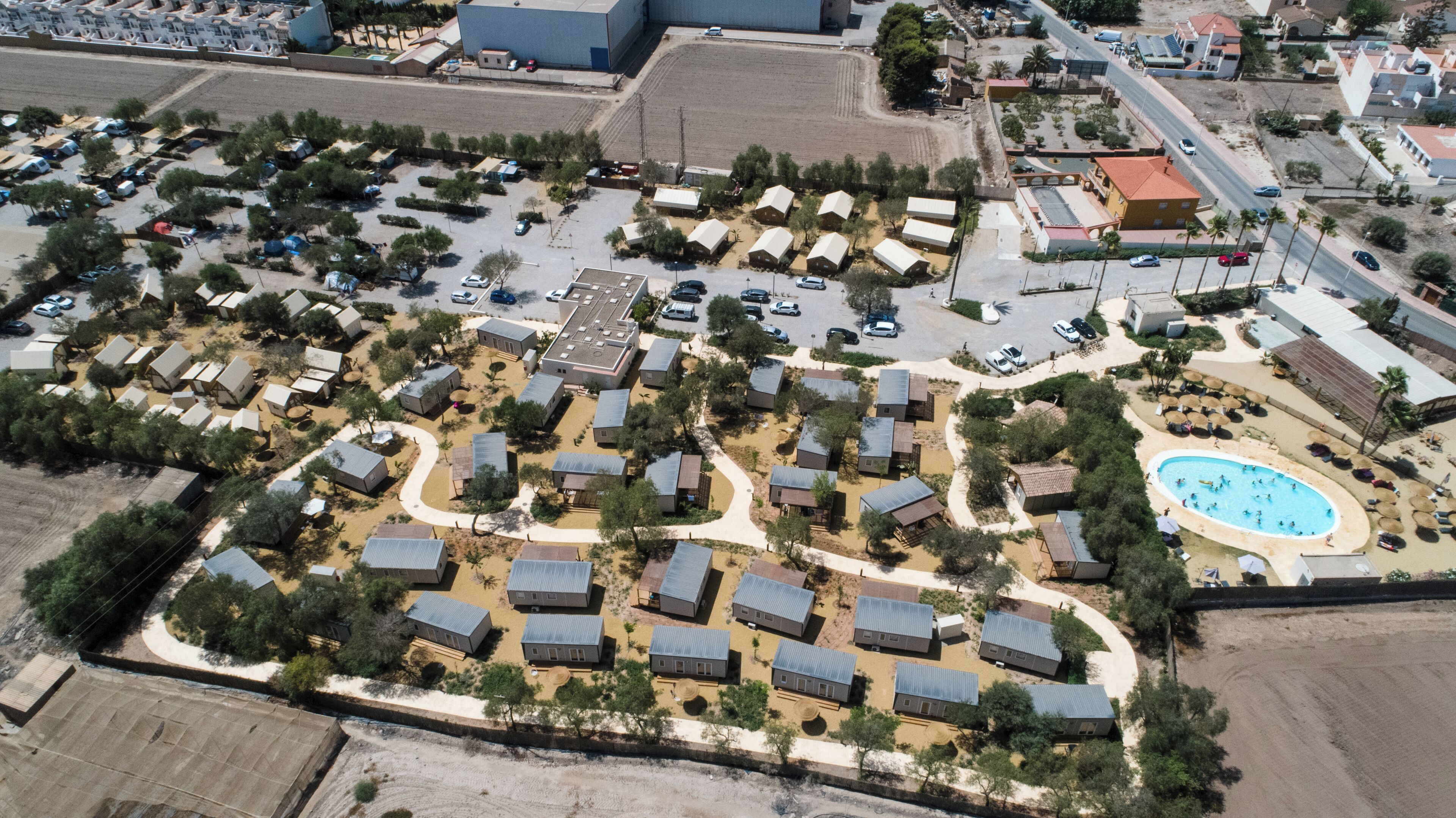 Vista aérea de un camping con varias cabañas, una piscina y un aparcamiento.