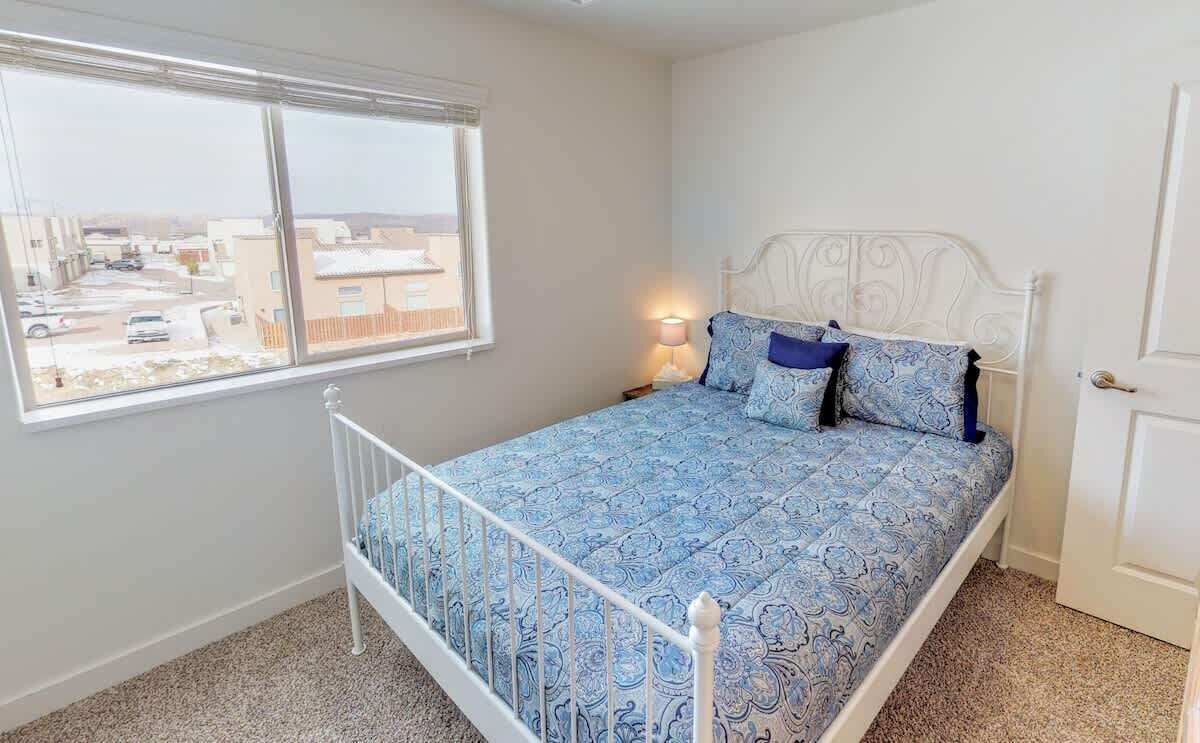 A bedroom with a bed, a window, a nightstand, and a door.