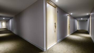 A hallway with carpeted floors and grey walls, featuring a wooden door with a handle and a small sign above it.