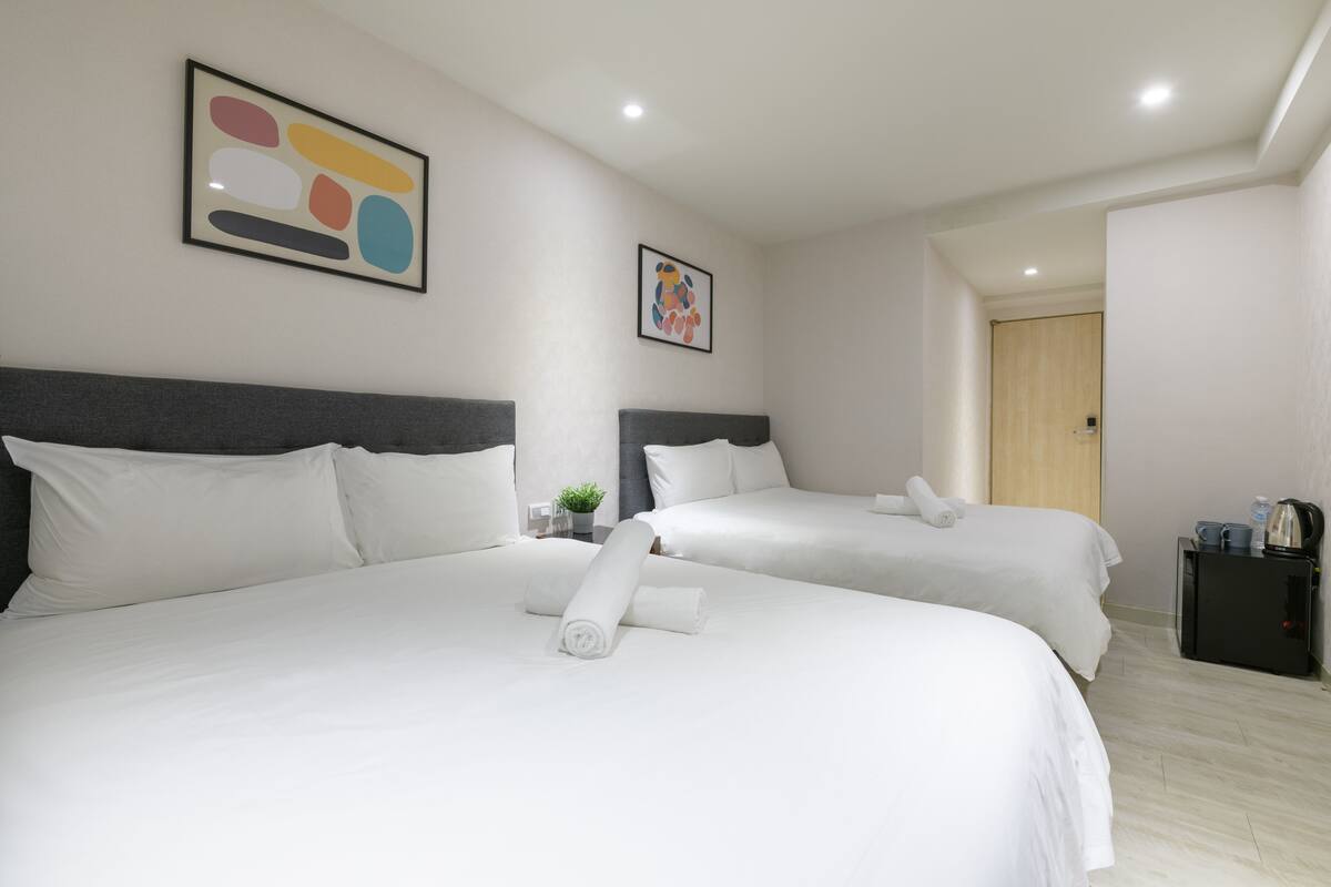 A hotel room with two beds, white bedding, a small table with a plant, and artwork on the walls.