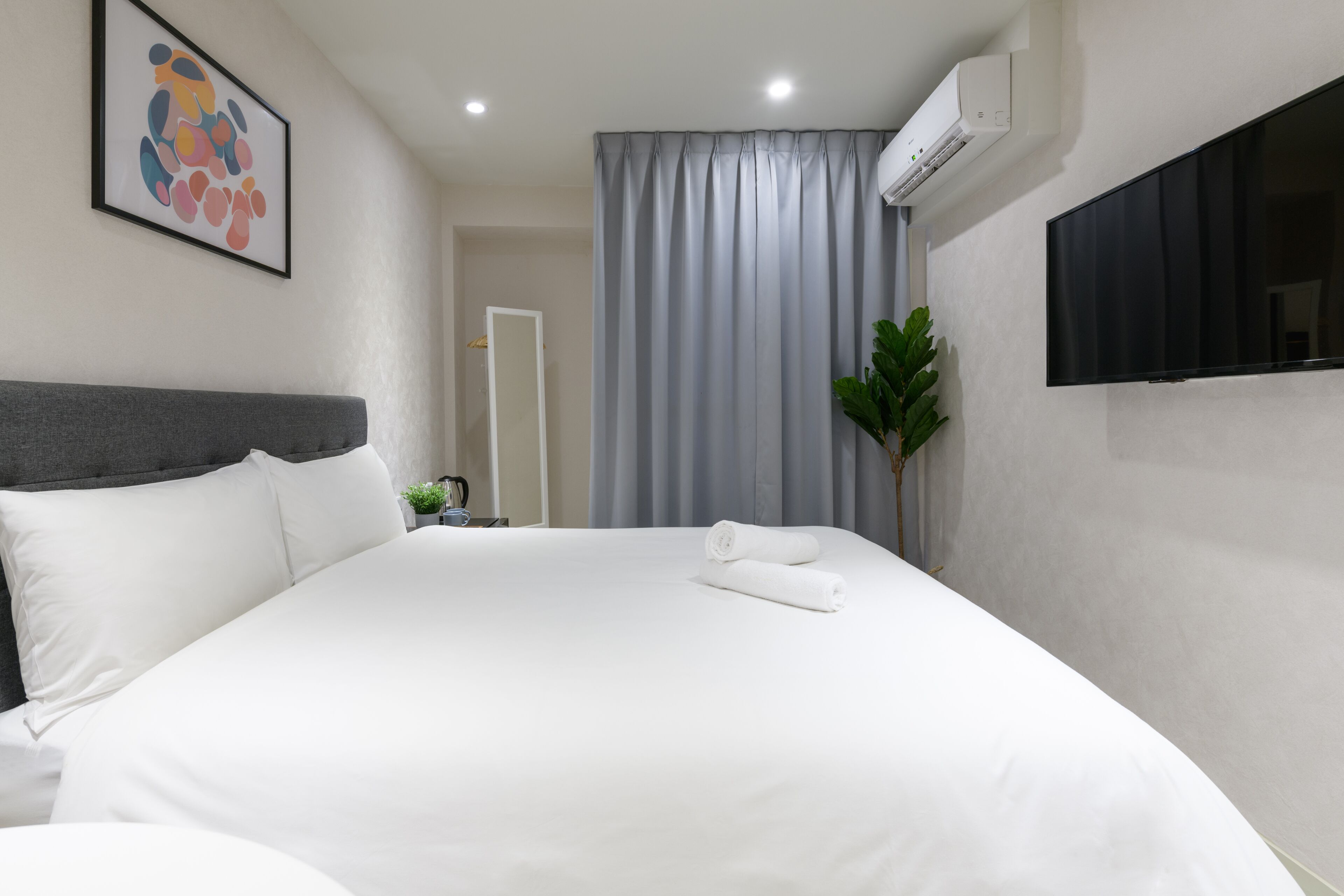 A neatly made bed with white linens, a grey headboard, and a grey curtain in the background.