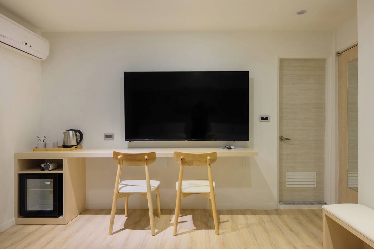 A modern room with a flat-screen TV mounted on the wall, two wooden chairs, a small refrigerator, and a wooden bench.