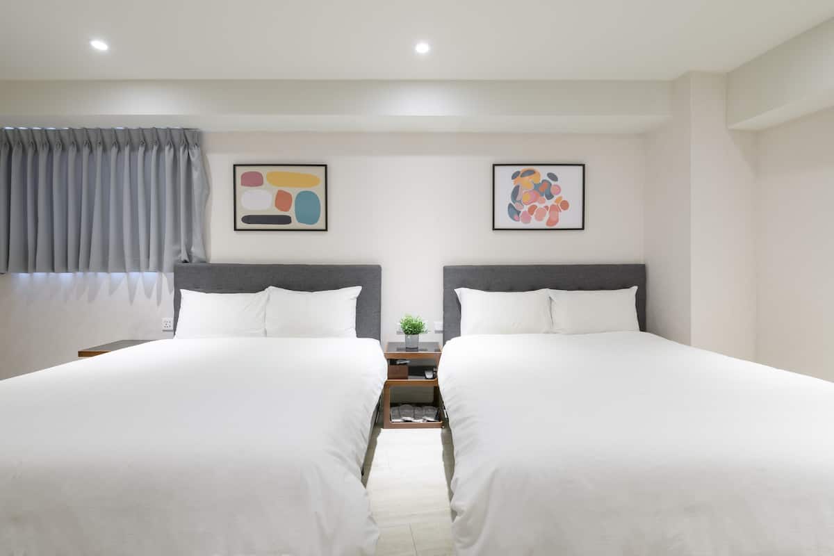 A hotel room with two beds, a nightstand, and two abstract paintings on the wall.