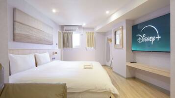 A hotel room with a large bed, a flat-screen TV mounted on the wall, a ceiling air conditioner, and a window with curtains.