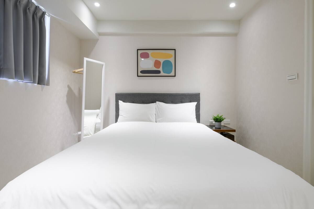A bedroom with a large bed, a bedside table with a plant, and a wall-mounted abstract art piece.