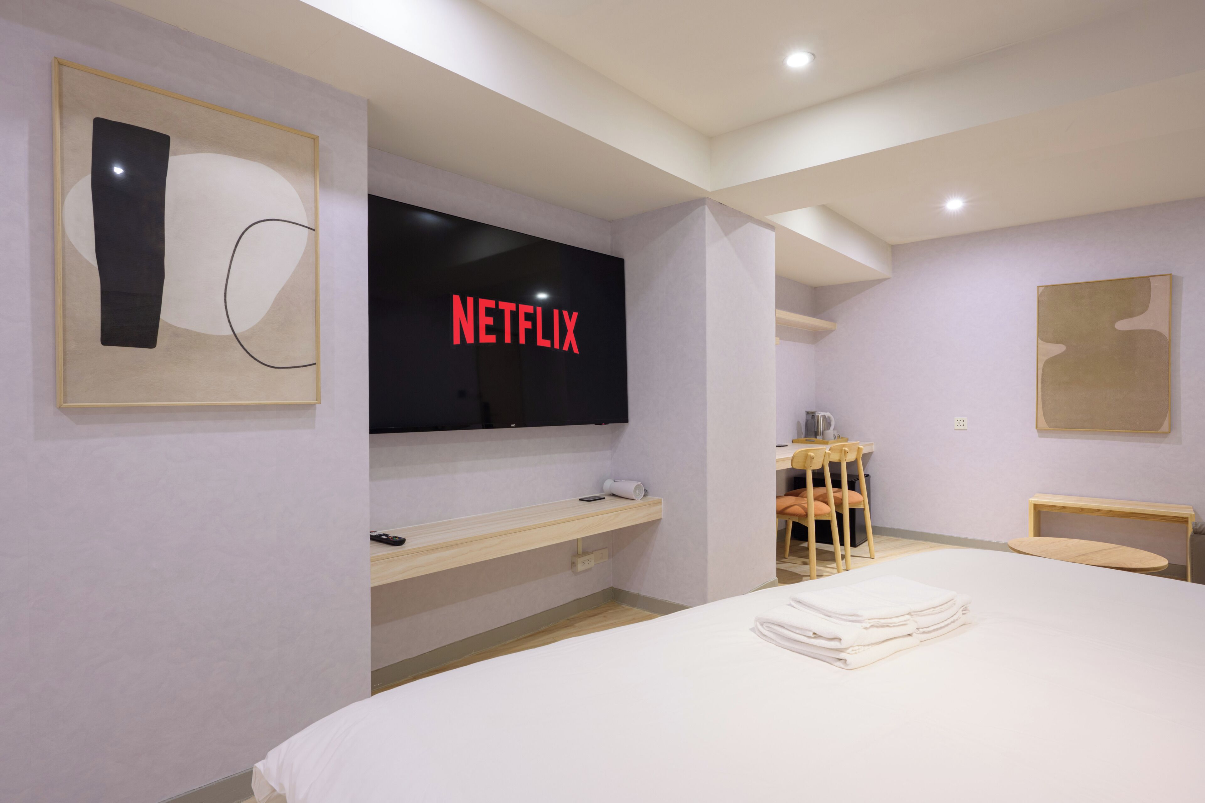 A modern hotel room with a large bed, a flat-screen TV mounted on the wall, a wooden desk, and a chair.