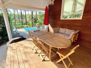 A wooden deck with a table and chairs, a red umbrella, and a pool in the background.