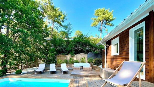 Un terrazzo in legno con piscina, sedie a sdraio e una casa di legno sullo sfondo.