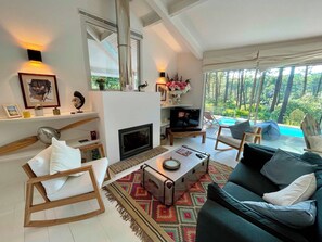 A modern living room with a fireplace, seating area, and a view of a swimming pool. - Attractive villa with pool in golf resort G0279 (Lacanau)
