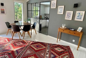 A dining area with a round table and chairs, a patterned rug, a wooden side table with a candle, and framed pictures on the wall. - Attractive villa with pool in golf resort G0279 (Lacanau)