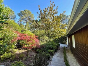 A garden with a wooden pathway leading to a house. - Attractive villa with pool in golf resort G0279 (Lacanau)
