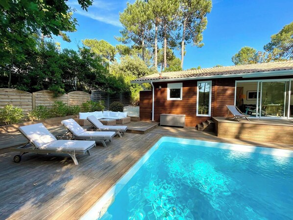 A swimming pool with lounge chairs, a wooden deck, and a small building with a tiled roof.
