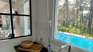 Una cucina con una ciotola di legno su un vassoio, una bottiglia di detersivo per piatti e una finestra vista piscina e foresta.
