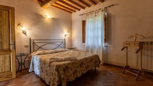 Ein Schlafzimmer mit Bett, Holzbalkendecke, einem kleinen Tisch, einem Stuhl, einem Nachttisch und einem Holzschrank.