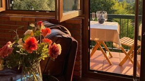 Habitación con vistas a un paisaje montañoso a través de amplios ventanales. Se observa una mesa con un florero y una silla.