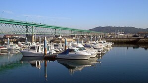 Un puerto deportivo con barcos amarrados bajo un puente verde.