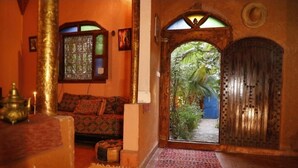 Un intérieur marocain traditionnel, avec une porte en bois, un canapé à motifs et une vue sur la verdure à l’extérieur.