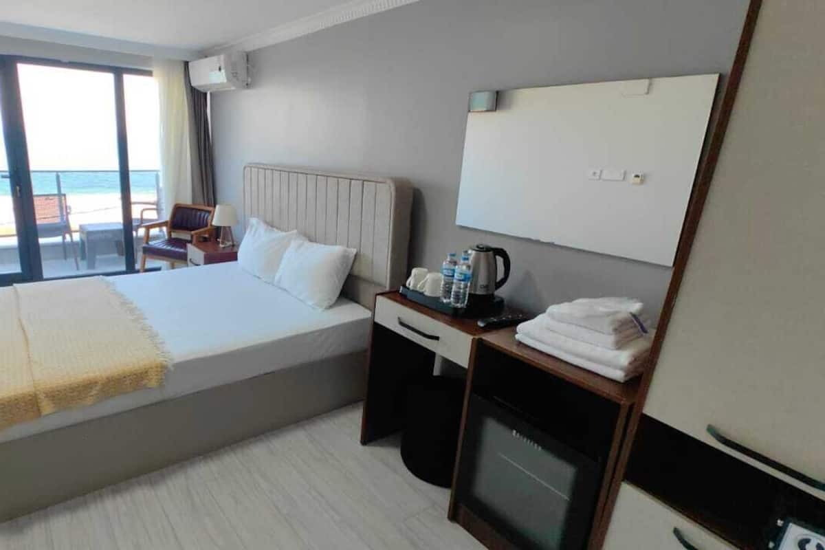 A hotel room with a large bed, a desk with a chair, a minibar, and a view of the beach.