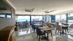 Un restaurant moderne offrant une vue sur la mer, avec un sol carrelé et un mobilier contemporain au design épuré.